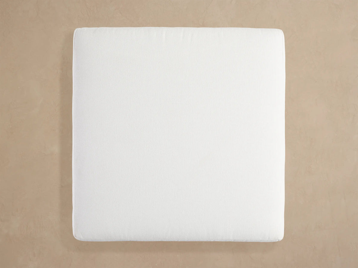 Angled close-up of Naxos Outdoor Ottoman. Thick white textured cushion sits on a dark gray rectangular metal frame.