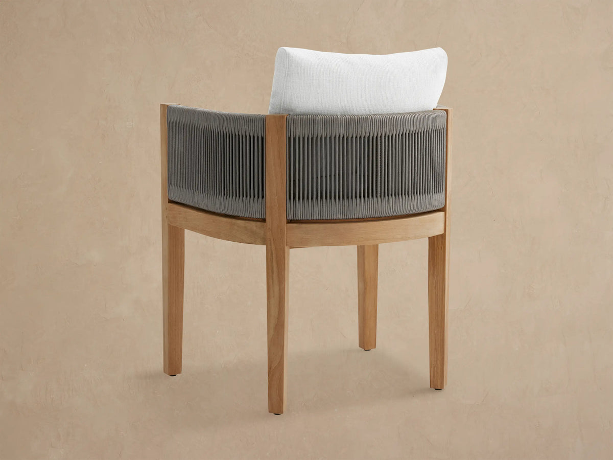 Newport Outdoor Dining Arm Chair, angled close-up. Teak wood frame, gray woven rope back, white Eden Snow cushions.