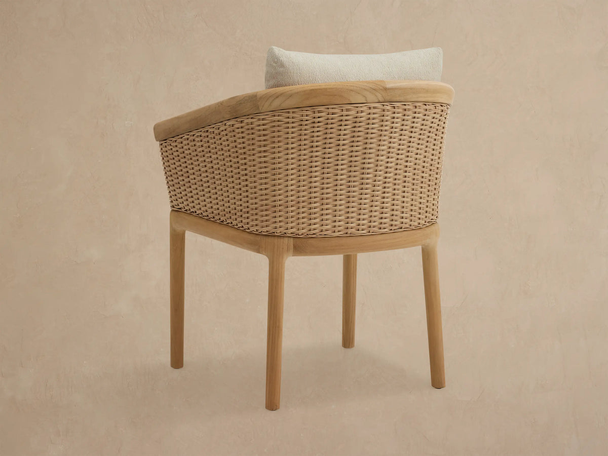 Puglia Outdoor Teak Dining Chair with natural teak frame, light brown woven sides, and cream-colored cushions.