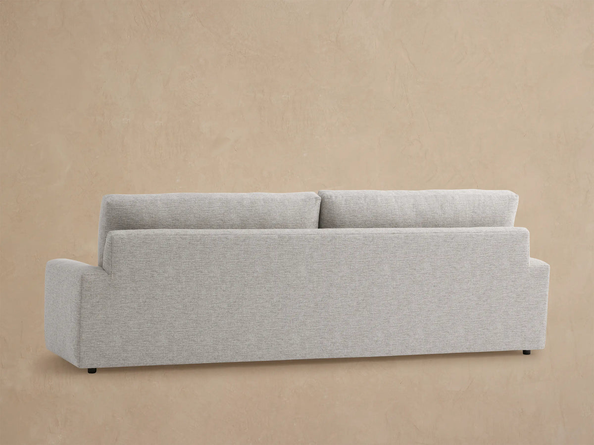 Remington Outdoor Sofa: Close-up of durable light gray textured fabric on armrest and backrest against a soft brown wall.
