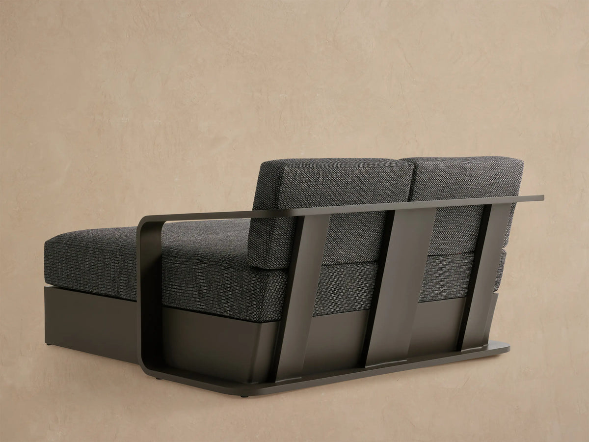 Sonoma Outdoor Aluminum Daybed close-up: dark grey frame, wide armrest, textured charcoal grey woven cushions.
