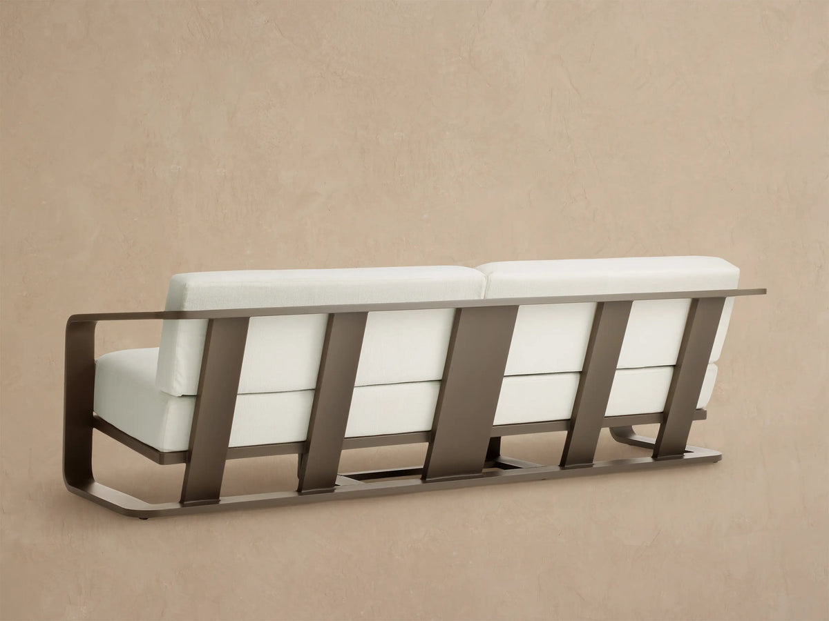 Angled close-up of Sonoma Outdoor Aluminum Sofa with curved dark bronze frame and plush white Savona Snow cushions.