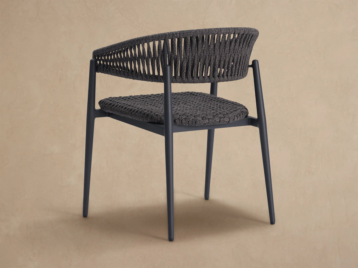 Close-up Talia Outdoor Dining Chair. Dark gray woven seat & open-patterned back. Black aluminum frame, neutral background.