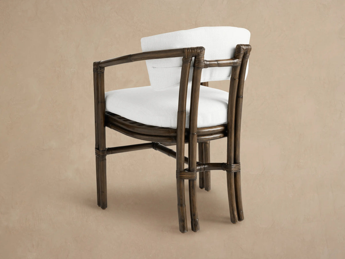Close-up of a Van Sunroom Dining Chair with dark brown rattan frame and plush white seat and back cushions, on a neutral background.