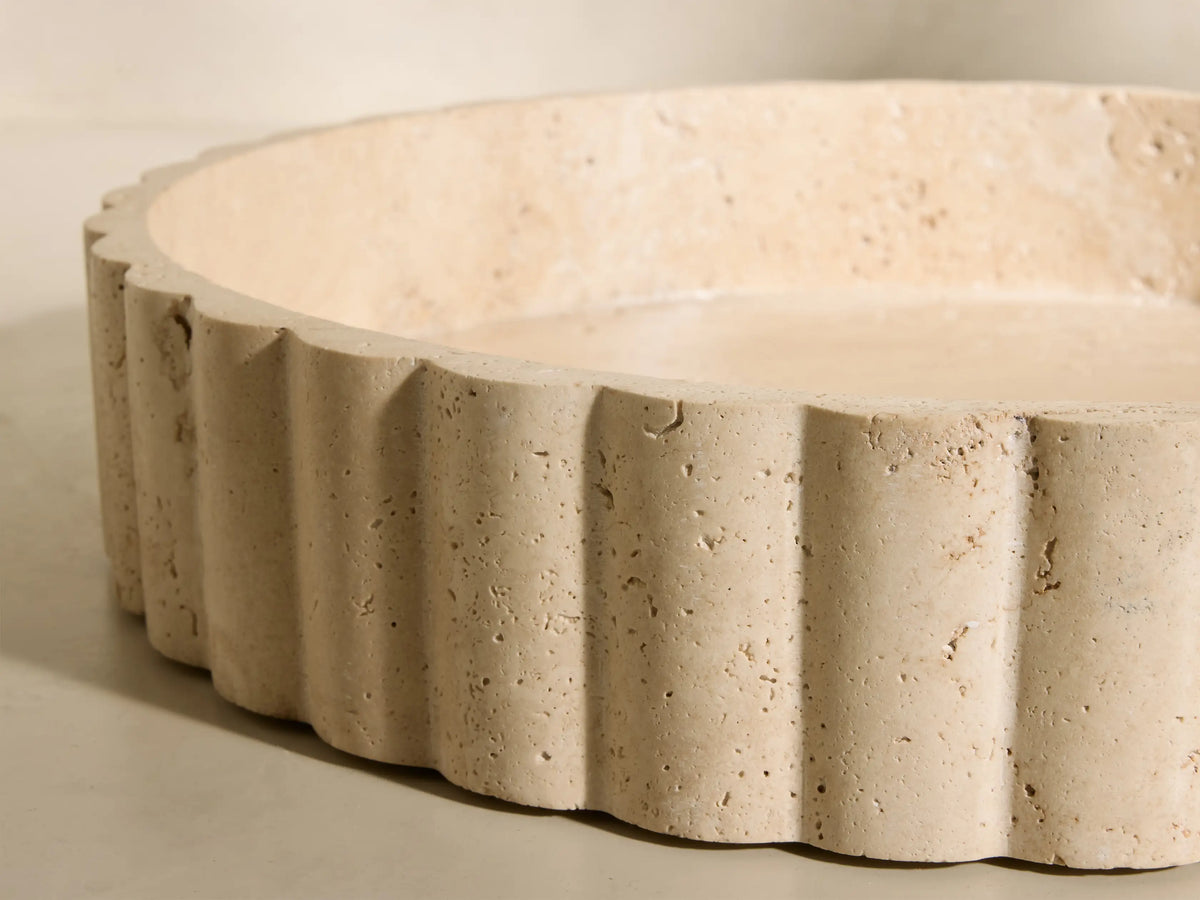 Front view of a beige and ivory-toned Sylvaine Tray, a round porous travertine stone tray with scalloped detailing.