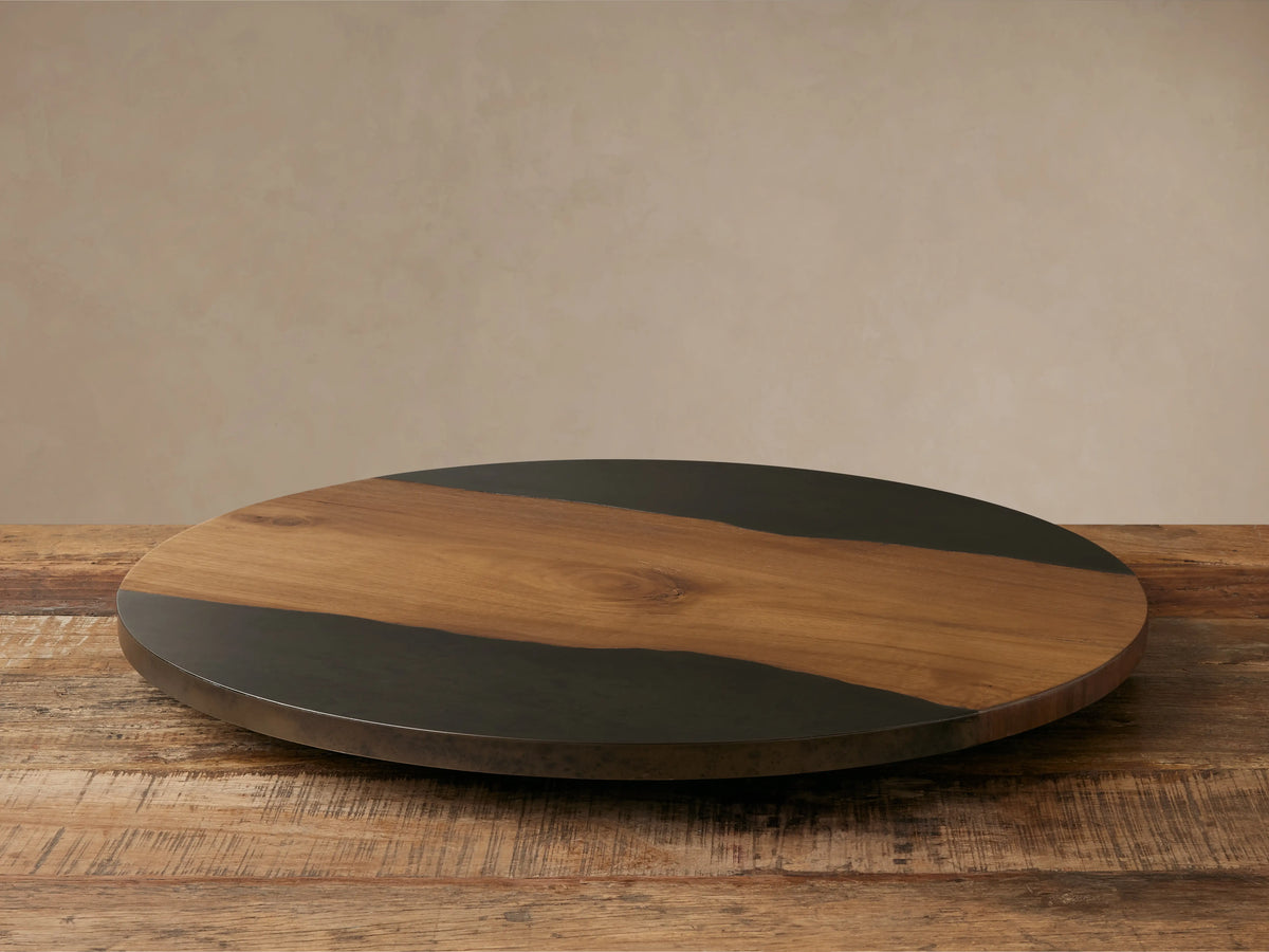 Acacius Lazy Susan: circular, featuring a wavy natural wood band flanked by dark oxidized steel, on a rustic wood table.