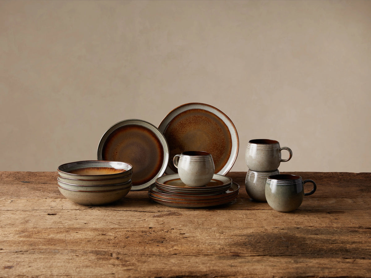 Canyon 16-piece dinnerware set: stacked pasta bowls, plates, and mugs with earthy, reactive brown & neutral glaze on wood.