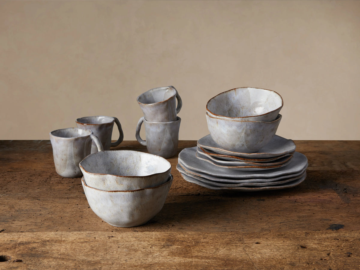 Skye Dinnerware set of 16, white glazed stoneware mugs, bowls, and plates with dark trim, on a rustic wooden table.