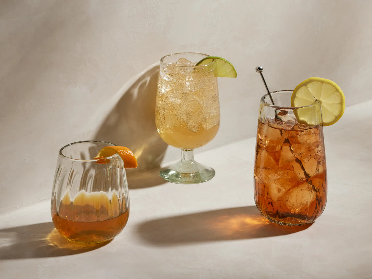 Seema Clear Highball Glass filled with an iced amber drink, garnished with a lemon slice on the rim and a silver stirrer.