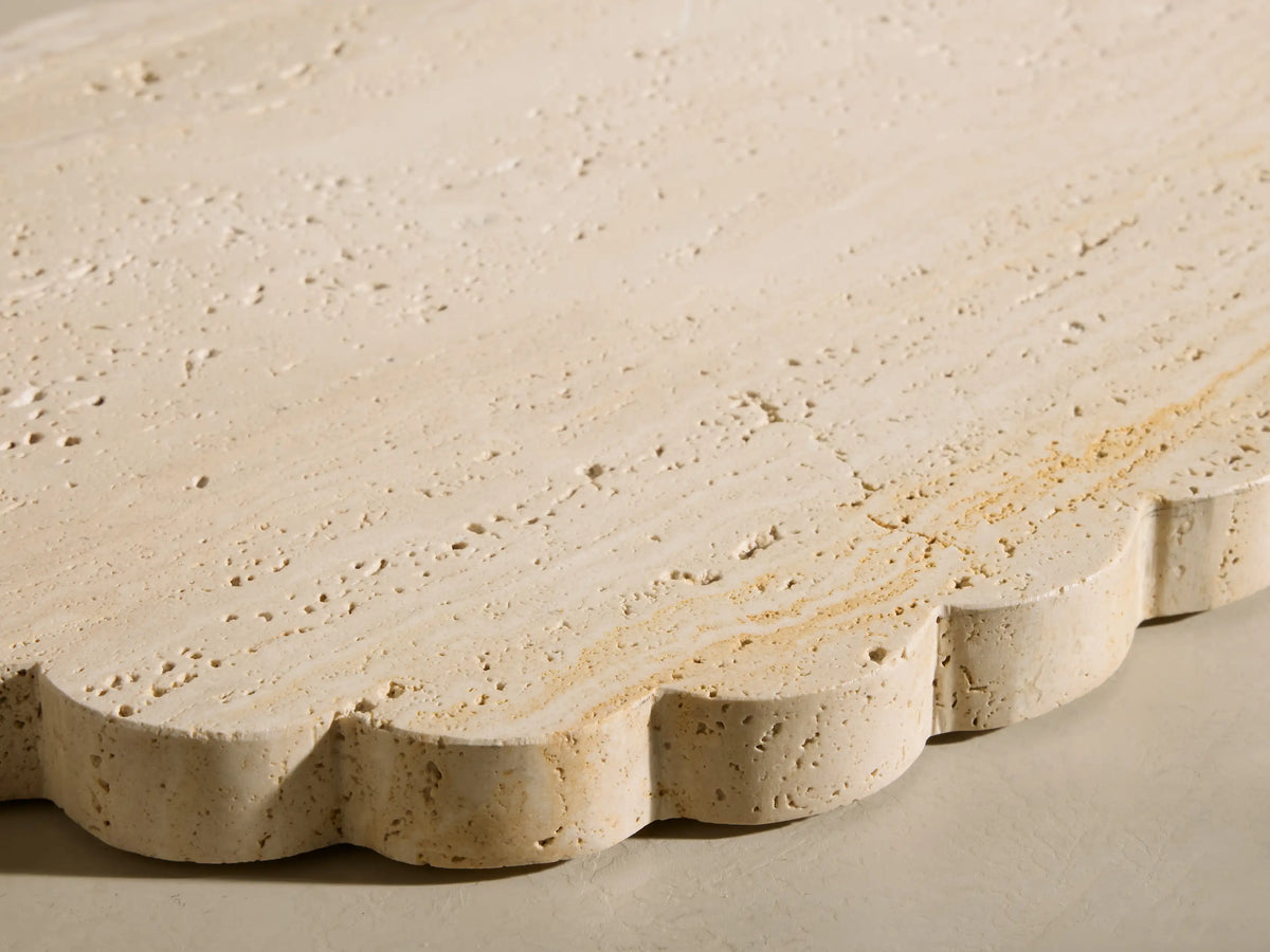 Angled view of the beige and ivory-toned travertine Sylvaine Oval Board, featuring scalloped edges and visible stone texture.