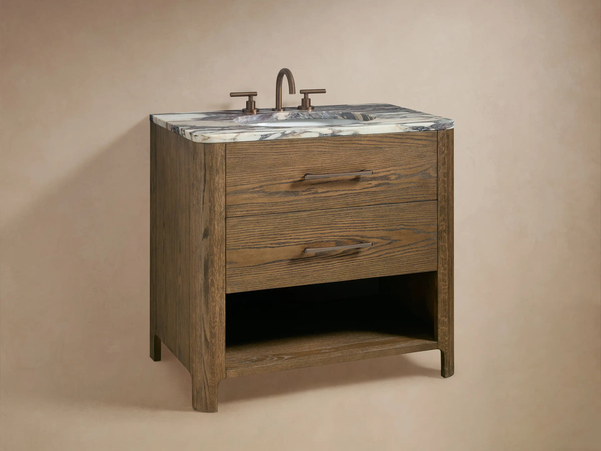 Calista Single Vanity open drawer: light brown oak wood grain, bronze handle. Inside, white towels, a dark organizer box, and a jar.