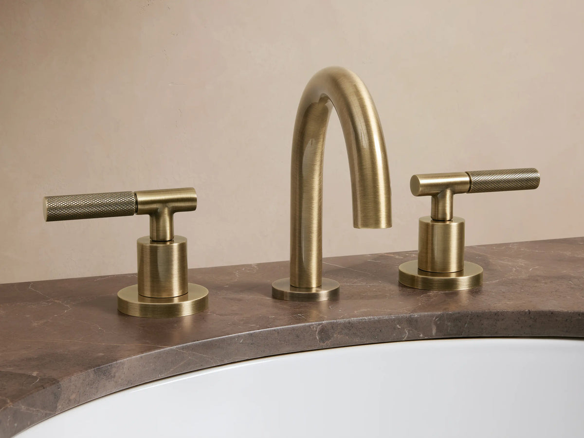 Crewe Knurled Faucet in antique brass finish with a curved spout and two cylindrical handles on a marble countertop.