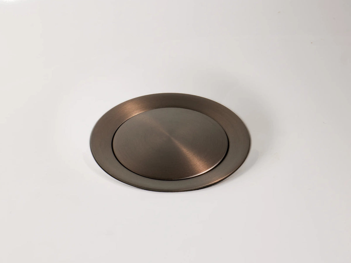 Bronze Crewe Knurled Faucet handle, T-shaped with textured grip, on a white marble surface, against a beige wall.