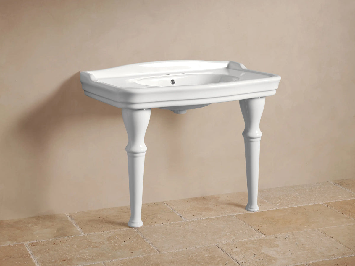 White Eloise Single Washstand with integrated sink, four elegant turned legs, and chrome faucets, against a light wall & tiled floor.