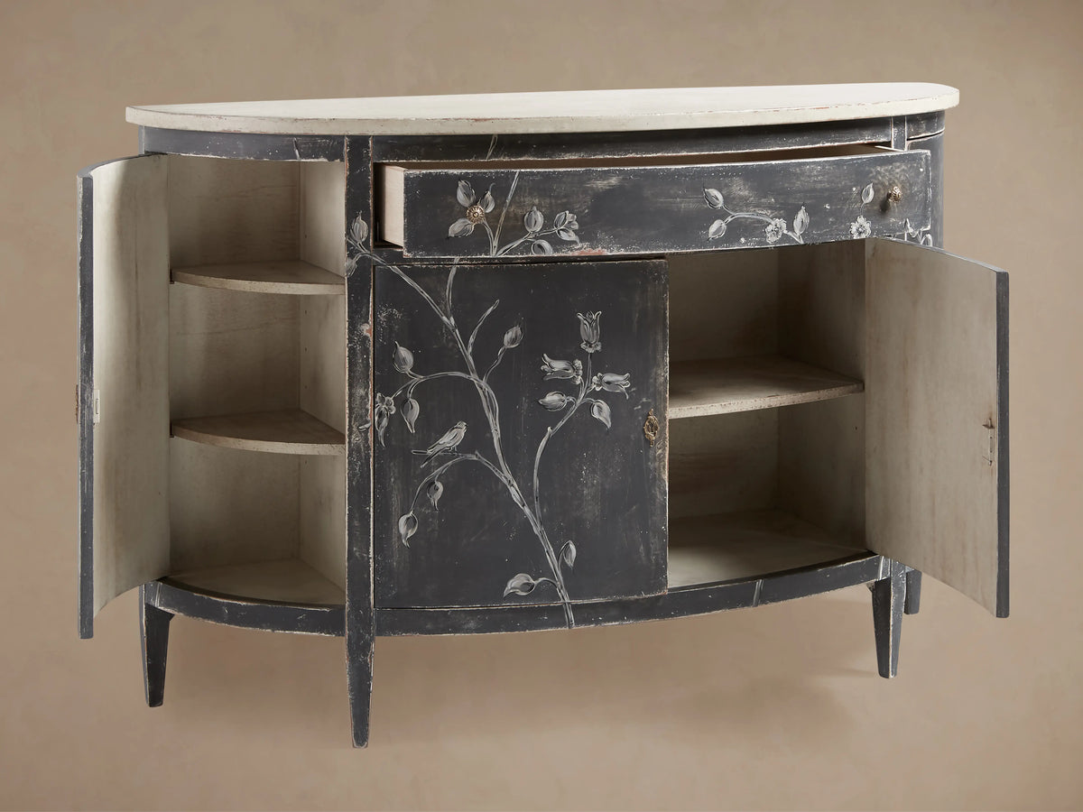 Sofia Bell'Arte Demilune Cabinet in profile view, featuring a dark, distressed finish with hand-painted floral motifs and a light-colored top.