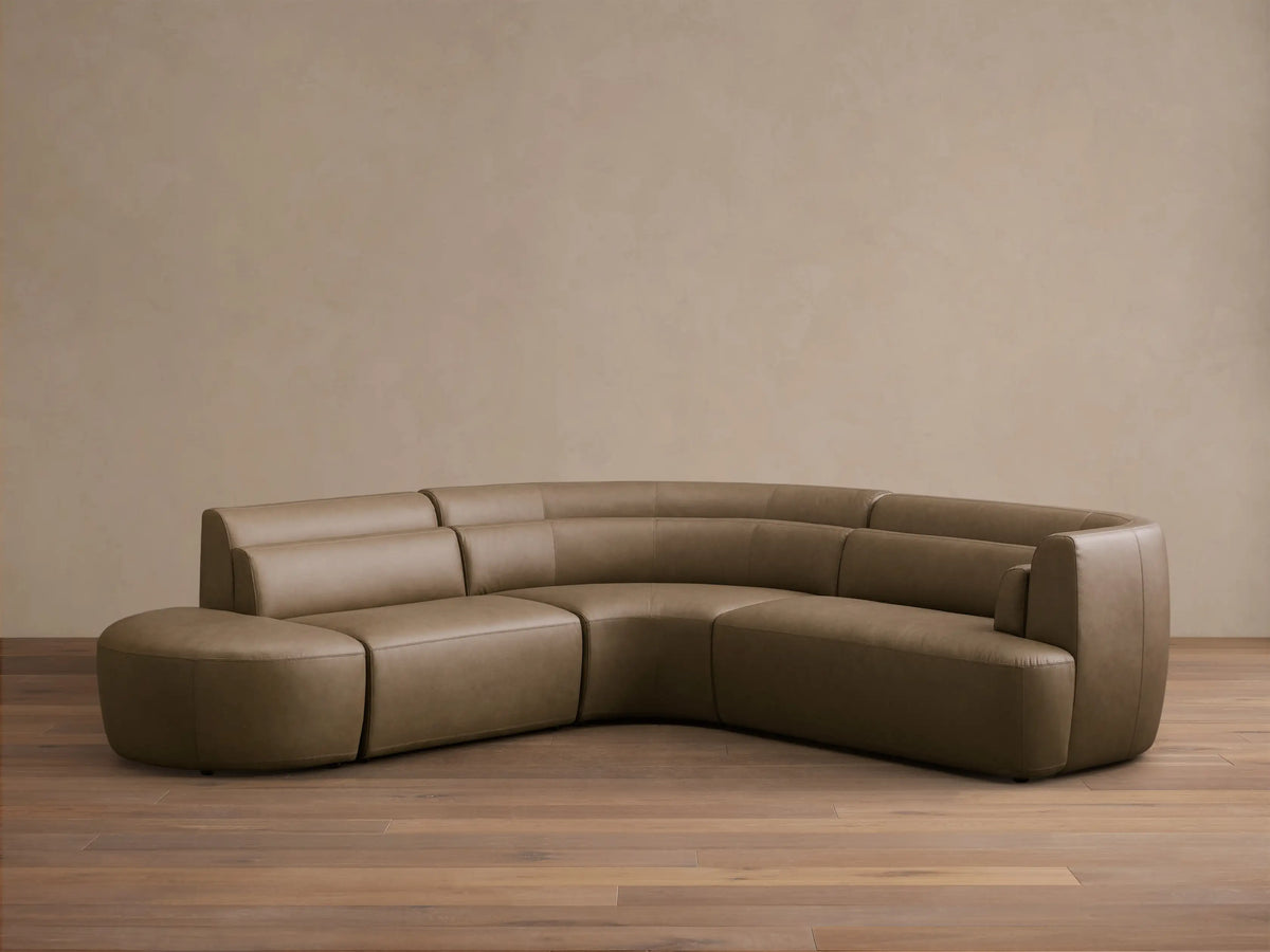 Rear view of the taupe Lovina Leather Four-Piece Sectional with Ottoman, showcasing its curved, segmented design.