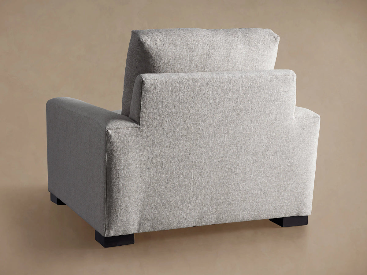 Rear view of a light grey upholstered Remington Chair with square arms and dark block feet.