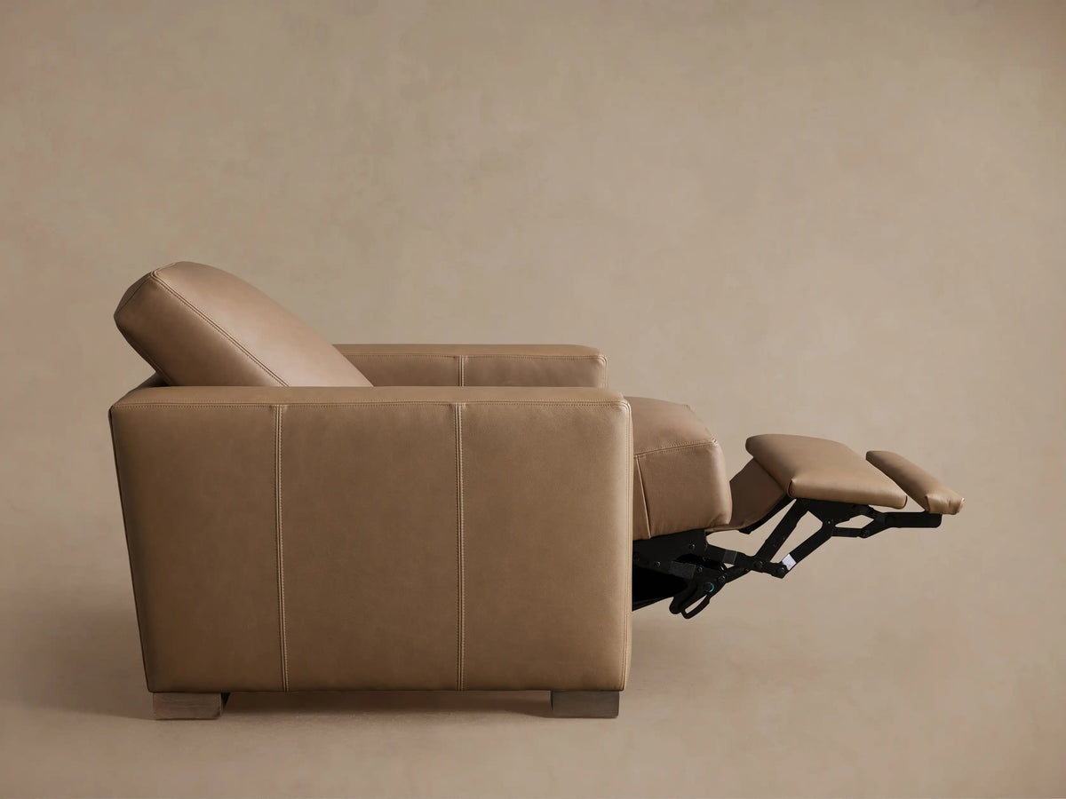 Remington Leather Motion Recliner in tan leather, angled view with footrest extended, against a light brown wall.
