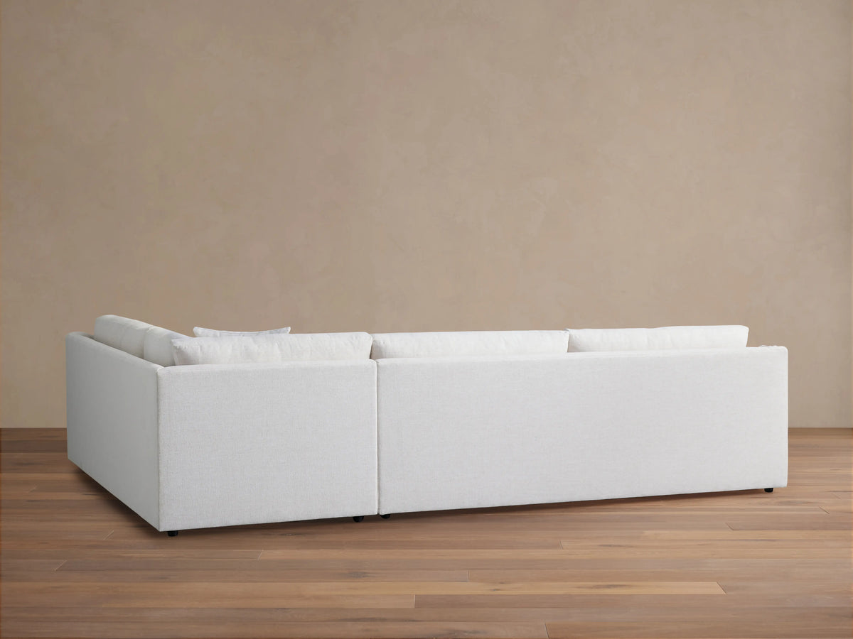 Ashby Two-Piece Sectional in pale fabric, seen from the back against a neutral wall. The sectional's linear design is visible on a wooden floor.