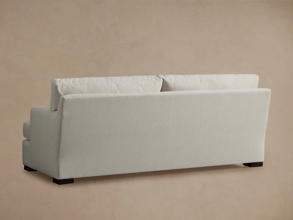 The image shows a close-up of the Dune Sofa's corner, highlighting its soft, textured, light-colored fabric and plush cushioning.