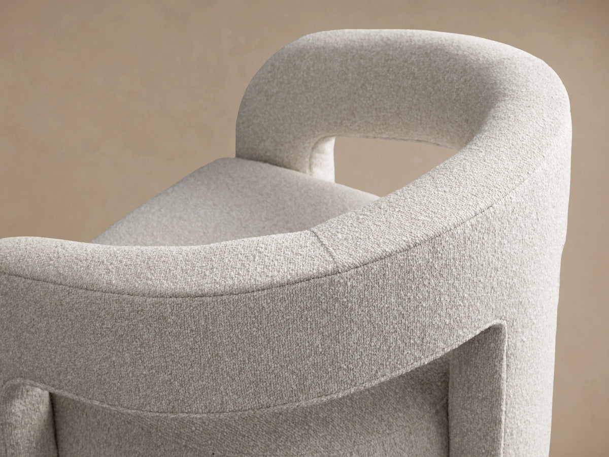 Light grey Mara Cutout Chair with textured fabric, modern curved arms and stout legs, angled on a wood floor.