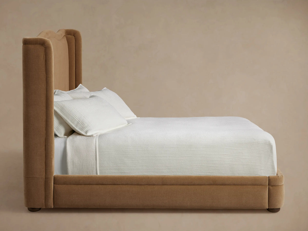 Close-up of the Winslet Bed's upholstered headboard, showing a curved corner in soft, warm brown velvet-like fabric.