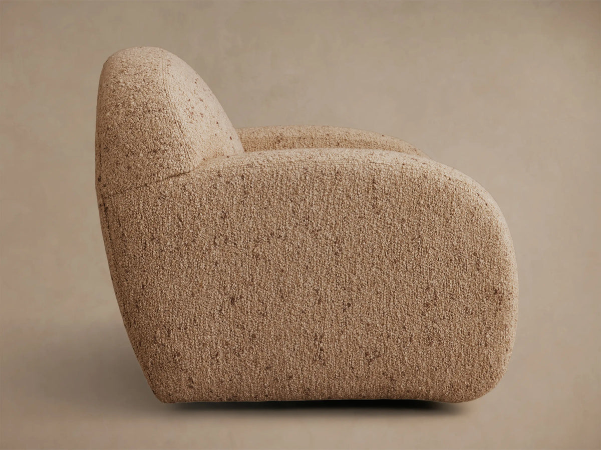 Side profile of the light brown textured Algiers Swivel Chair, featuring a rounded back and armrest.