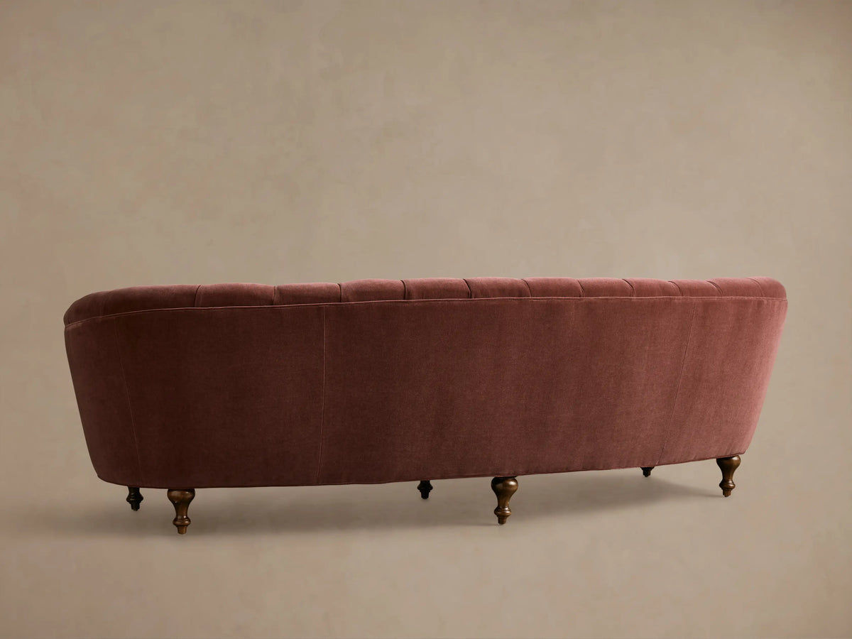 Close-up of the Rose Velvet Cortland Sofa, featuring a tufted curved back, smooth curved seat, and a turned mocha wooden leg.
