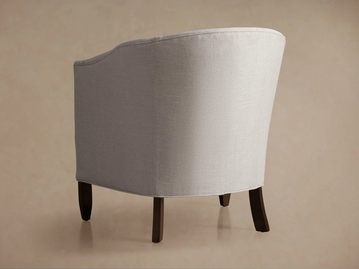 Giles Chair, close-up of its curved back and armrest in light gray textured fabric against a muted background.