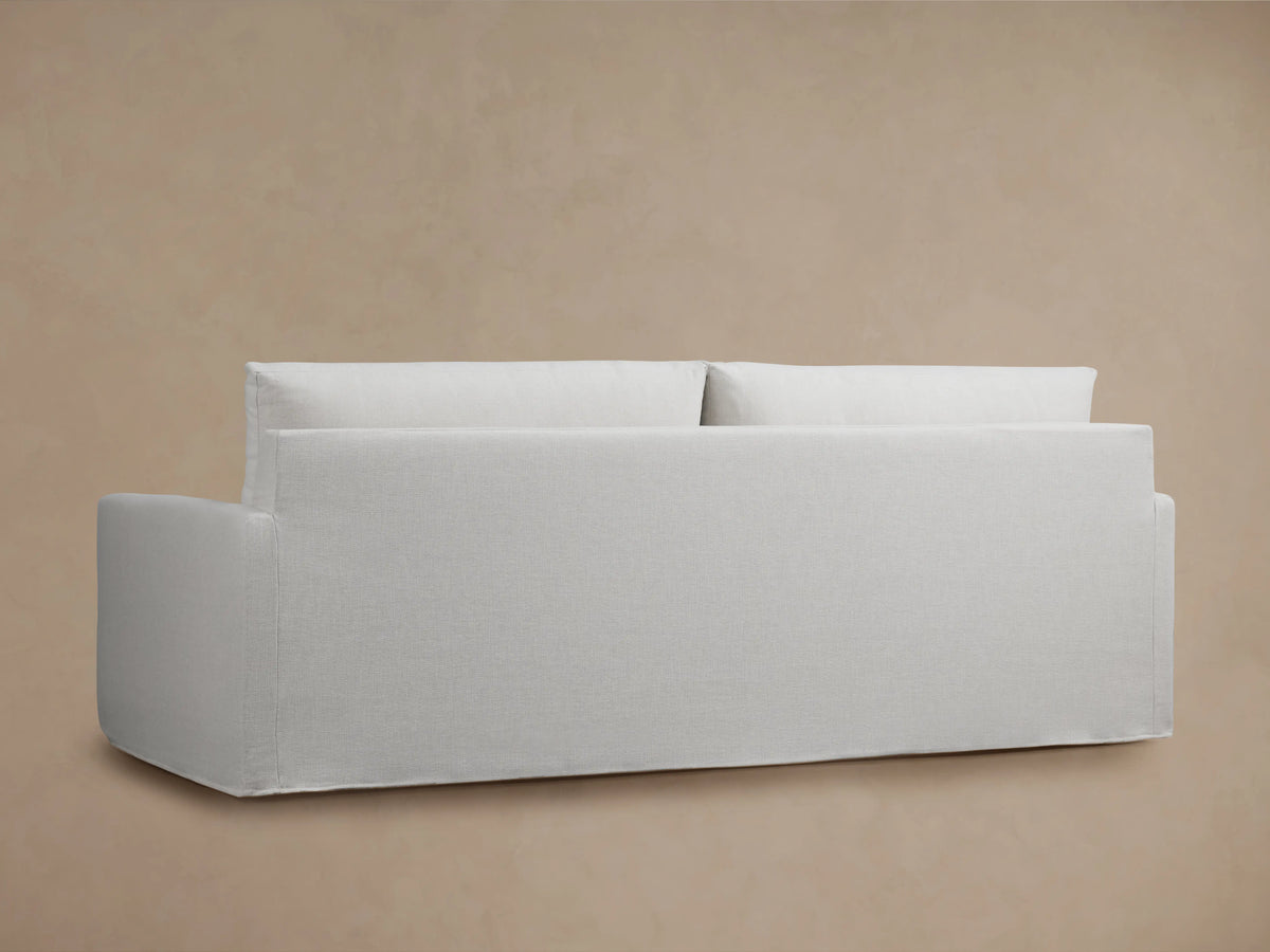 Close-up view of the Kipton Slipcovered Sofa showing its light beige fabric with soft, padded seat and back cushions.