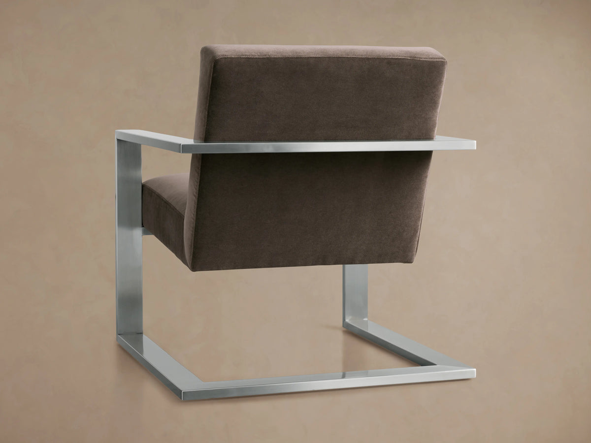 The Sabina Chair features a plush taupe cushion with a sleek metal frame. The thick cushion sits snugly between the metallic armrests.