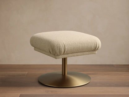Front view of a square beige fabric upholstered ottoman with a golden pedestal base on a wooden floor.