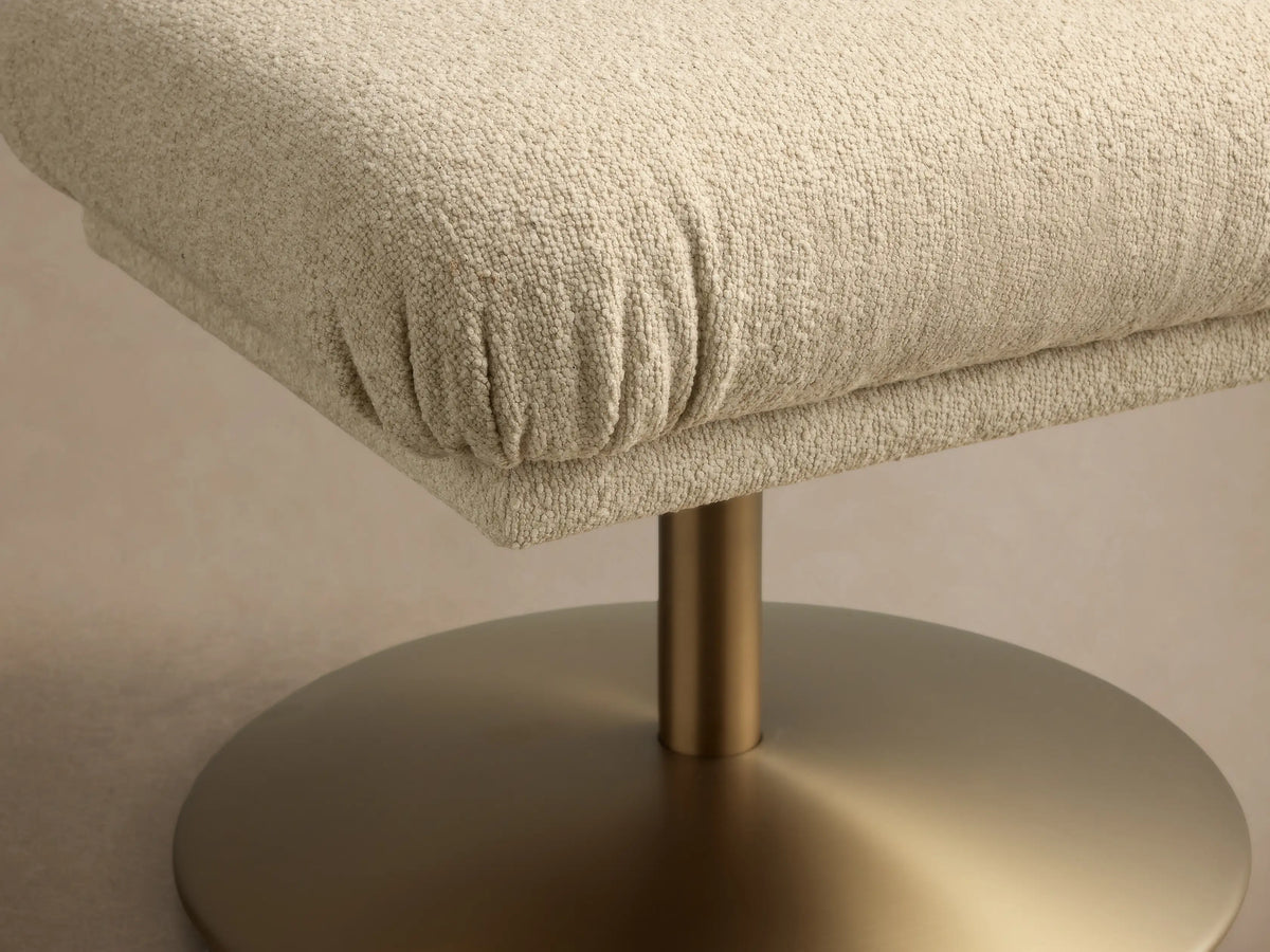 Front view of a light beige textured ottoman with a softly gathered cushion and a round, metallic bronze base.