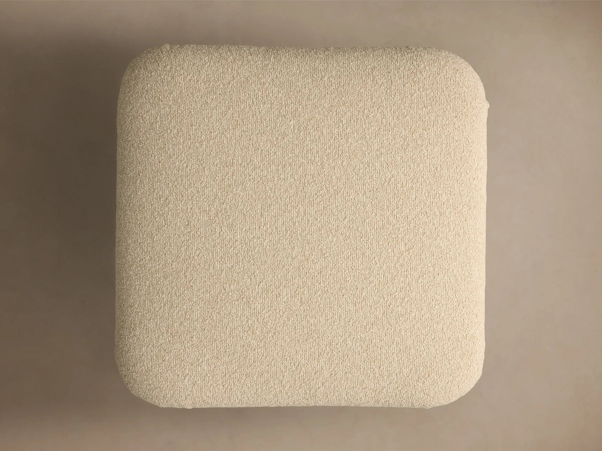 Close-up of a creamy beige textured cushion with subtle pleating, on a round, brushed bronze metallic base.
