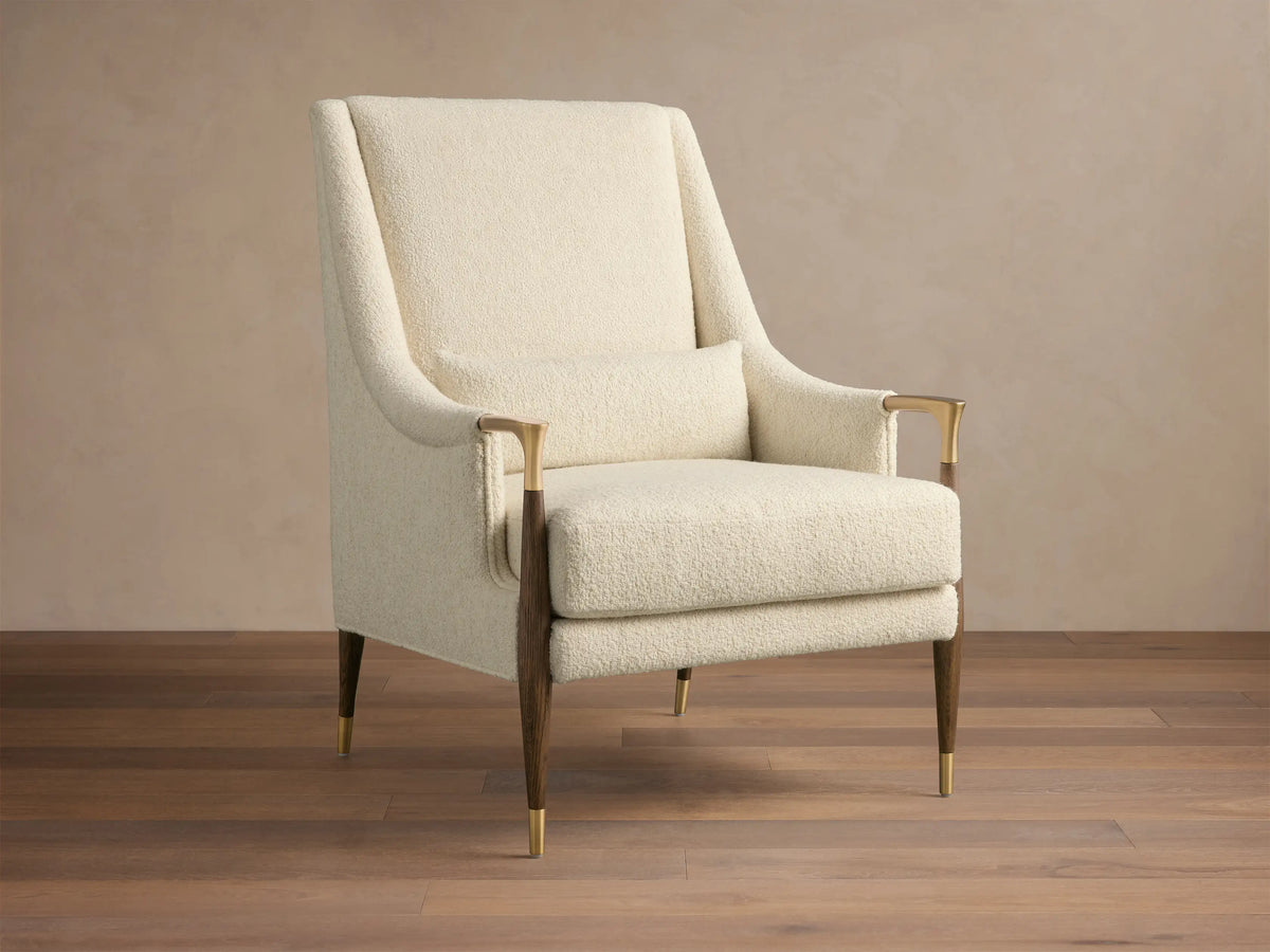 Front-right view of the cream textured Fisher High-Back Chair with dark wood legs, brass accents, and a lumbar pillow.