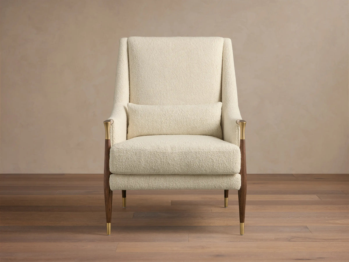 Front-right view of the cream textured Fisher High-Back Chair with dark wood legs, brass accents, and a lumbar pillow.