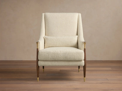 Front-right view of the cream textured Fisher High-Back Chair with dark wood legs, brass accents, and a lumbar pillow.