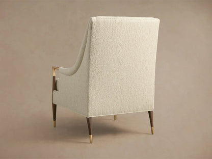 Close-up of the cream-colored Fisher High-Back Chair, featuring textured upholstery, brass armrests with dark wood, and a lumbar pillow.