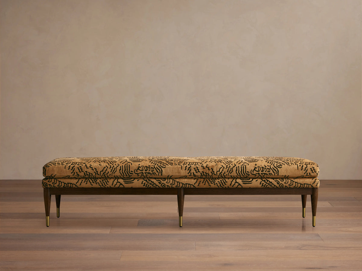 Fisher Bench with mocha-finished red oak frame, camel-colored cushion with abstract black pattern, set on a wooden floor.