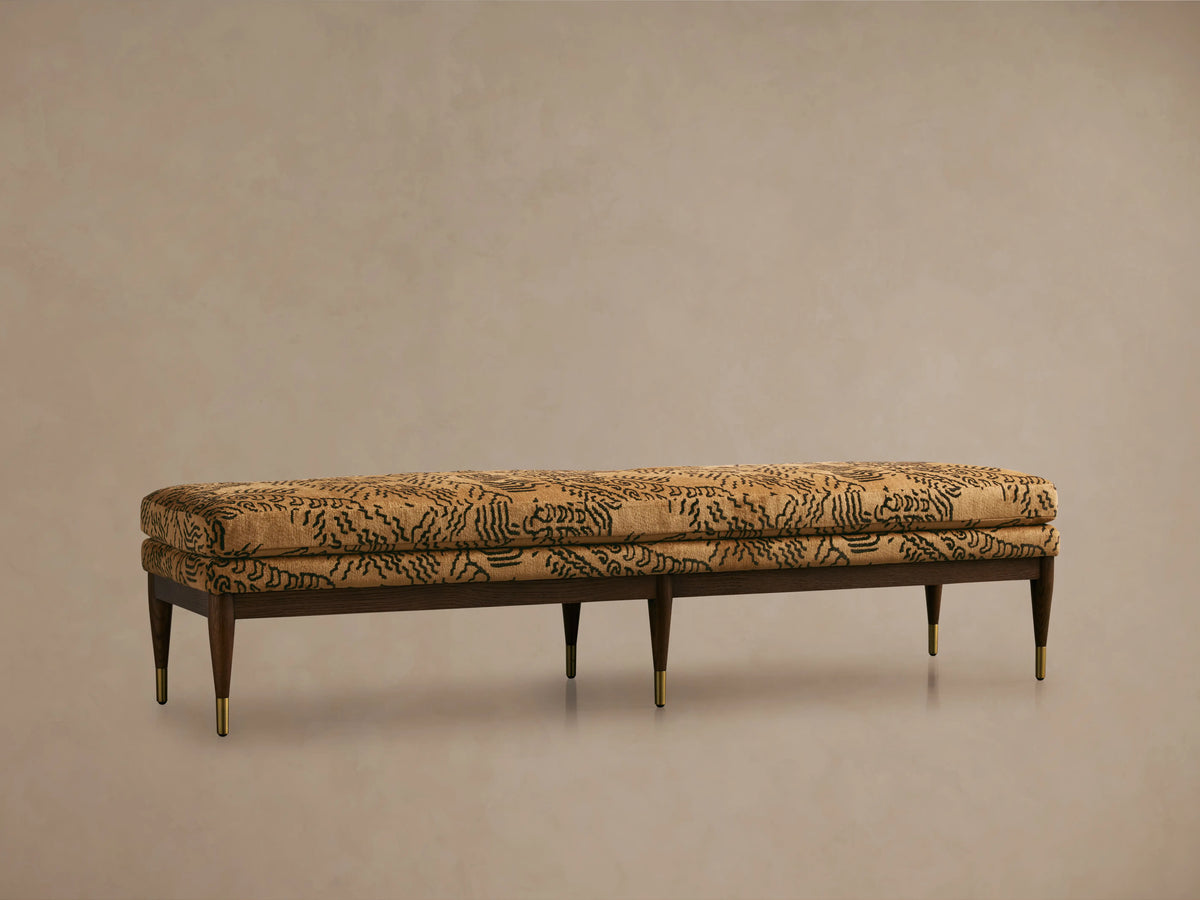 Fisher Bench with mocha-finished red oak frame, camel-colored cushion with abstract black pattern, set on a wooden floor.