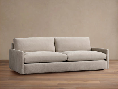 Kipton Sofa with a neutral beige fabric, featuring square arms and two large plush back cushions. The sofa is placed on a wooden floor.