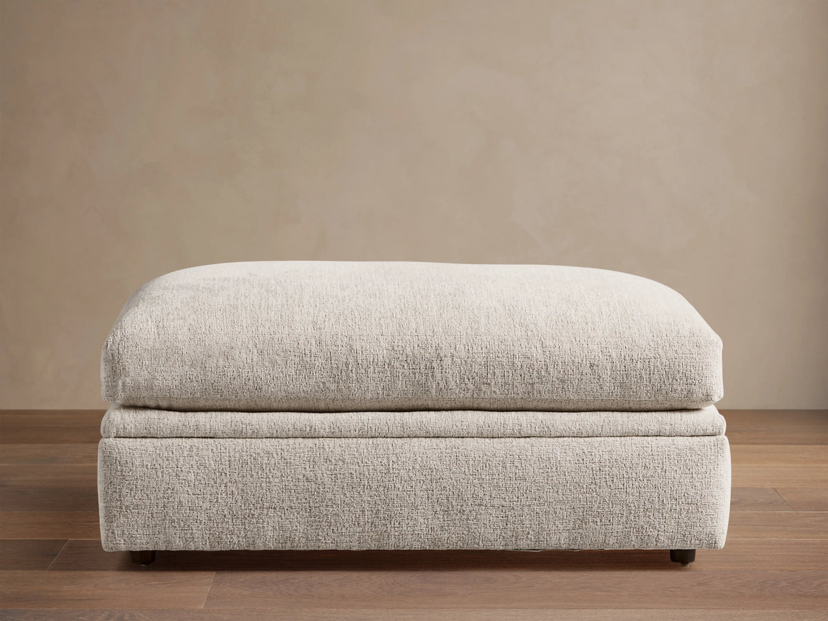 Light beige textured Kipton Storage Ottoman, rectangular with soft, rounded cushion top, on wood floor.