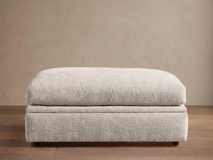 Light beige textured Kipton Storage Ottoman, rectangular with soft, rounded cushion top, on wood floor.