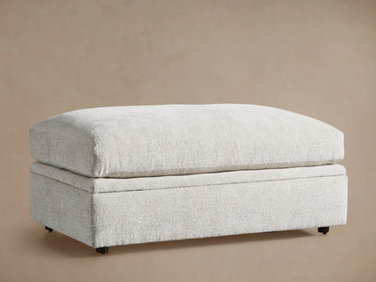 Light beige textured Kipton Storage Ottoman, rectangular with soft, rounded cushion top, on wood floor.