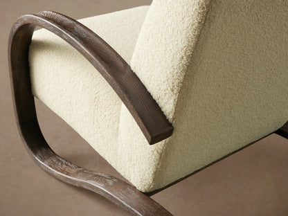 Allora Chair with curved mocha-finished red oak frame, beige fabric seat, and backrest. Positioned on a wooden floor.