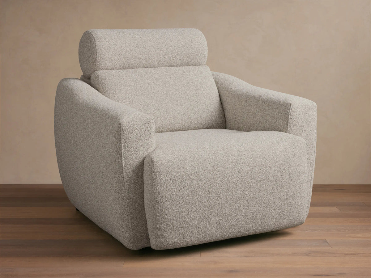 Front-quarter view of a light grey textured Fia Motion Recliner with wide arms and a padded headrest.
