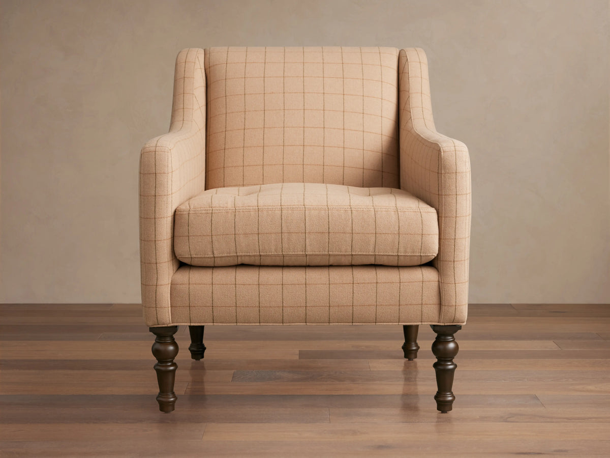 Tan plaid Fenwick Chair with a high backrest, cushioned seat, and curved arms on dark turned wooden legs, on hardwood floor.