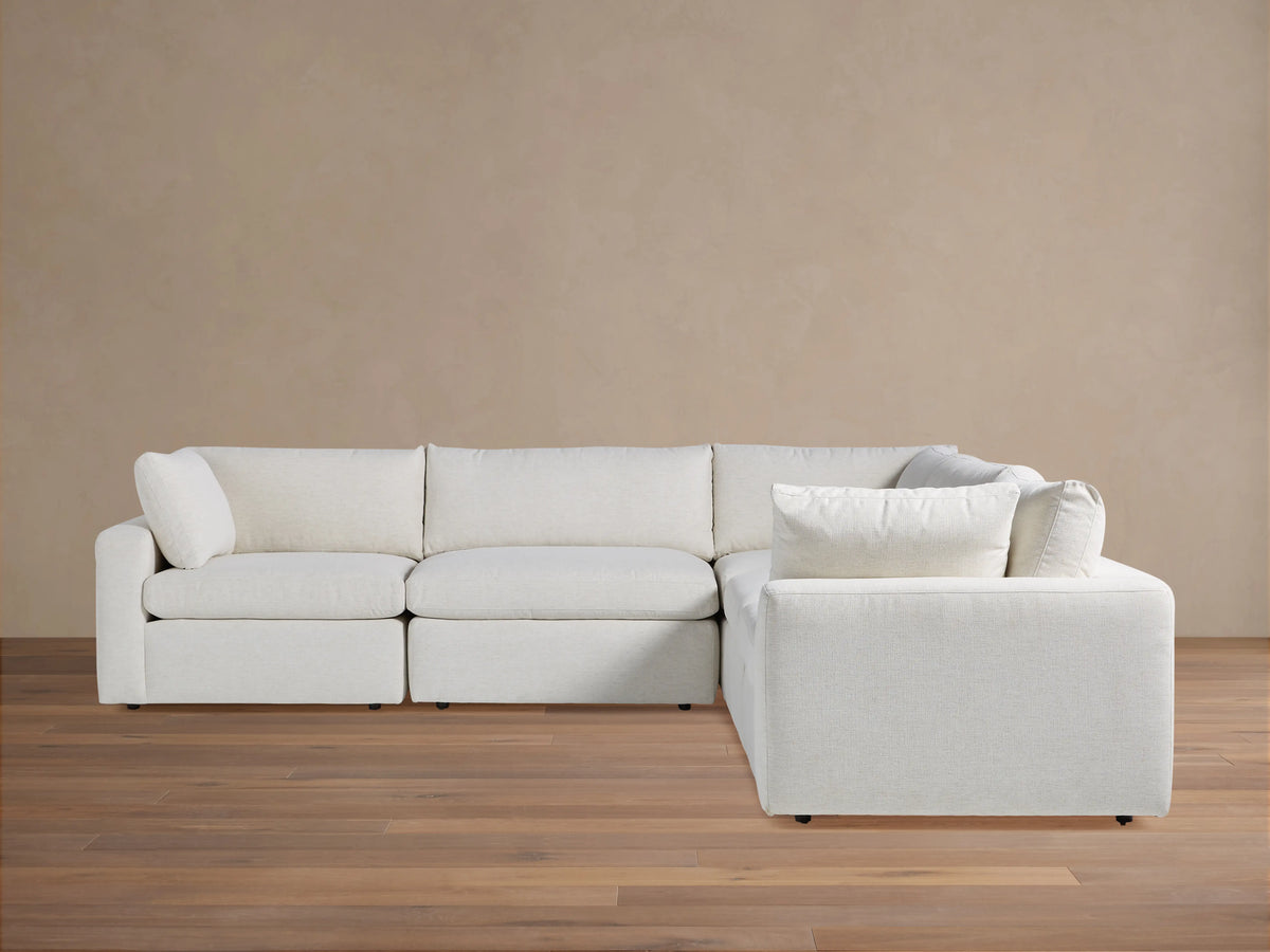 Beale Five-Piece Corner Sectional in off-white fabric, L-shaped with plush cushions, on wooden floor against a beige wall.