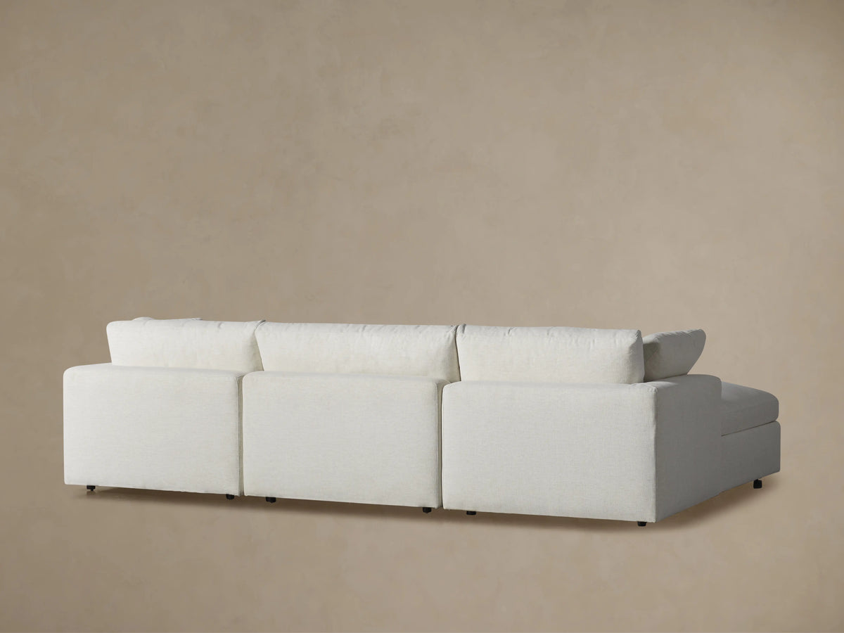 Side profile of a Beale Four-Piece Sectional in textured light fabric, showing a plush ottoman and deep, soft cushions.