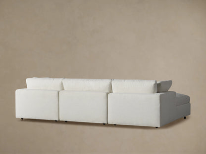 Side profile of a Beale Four-Piece Sectional in textured light fabric, showing a plush ottoman and deep, soft cushions.